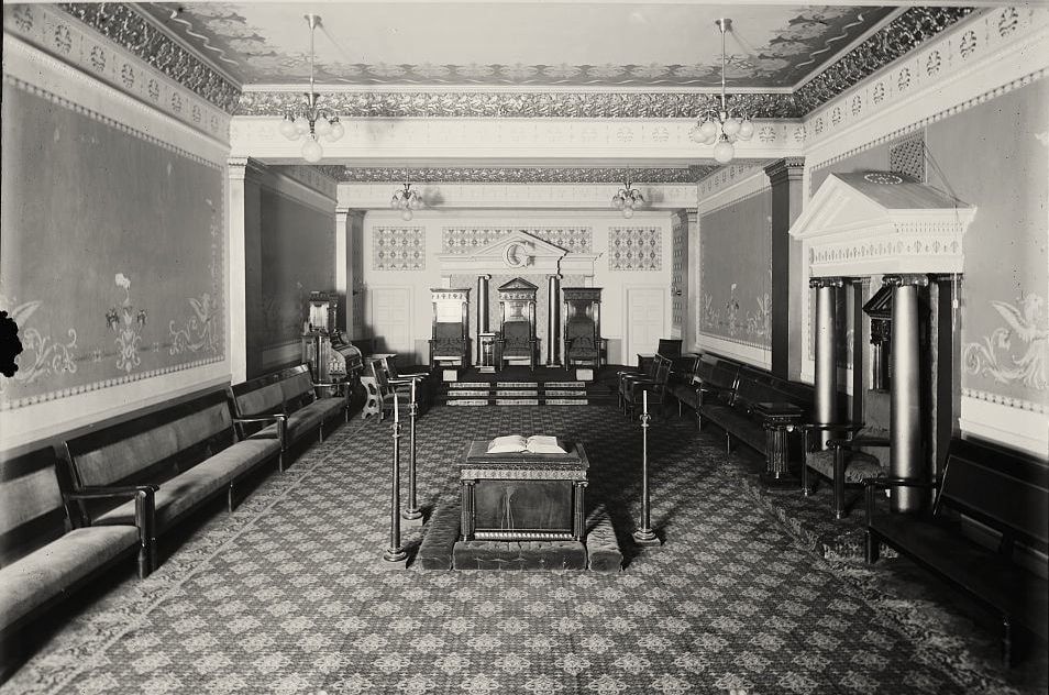 Photograph of a lodge room with patterned carpet, a central altar and a dais beneath the letter G.