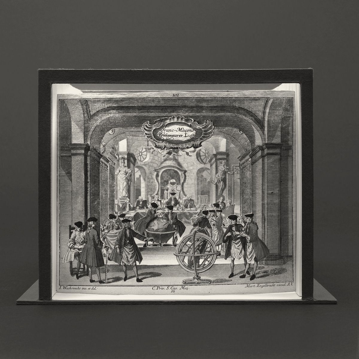 Photograph of a layered paper theatre: cut-out figures around a table and globe inside a receding room.