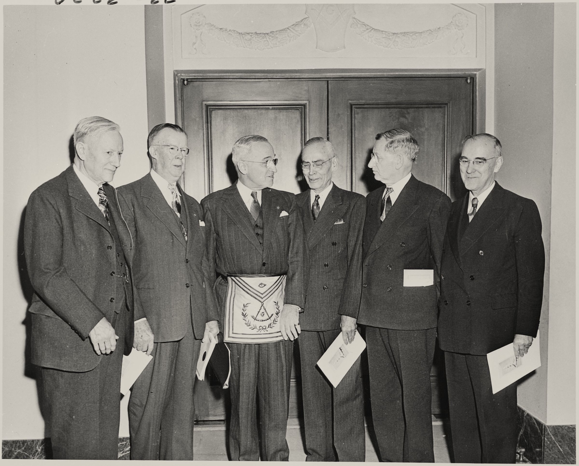 Harry S. Truman in a Masonic apron standing with five men in suits.